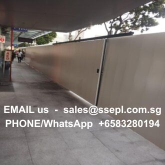 Concrete sidewalk blocked by a tall metal construction barrier; large white text on the barrier reads contact info: 'EMAIL us - sales@...com.sg' and 'PHONE/WhatsApp +65 3280 194' indicating how to reach for inquiries.